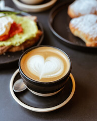 Cafe con dibujo de corazon en una taza y plato negro, con galletas en el desayuno