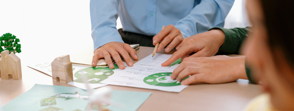 A cropped picture of green city poster was placed at green business meeting on meeting table with environmental document, wooden house block and windmill model scattered around. Closeup. Delineation.