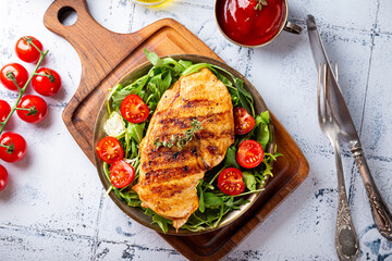 Grilled chicken breast with arugula and tomatoes on a plate top view