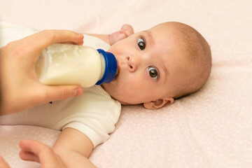 The baby drinks milk from a bottle. Feeding the baby with infant formula.
