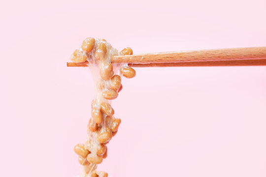 Japanese fermented natto beans on wooden chopsticks on pink background.