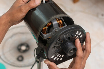 A technician removes the front casing to reveal and inspect the motor of an oscillating electric fan. Cleaning and repairing an electric stand fan.