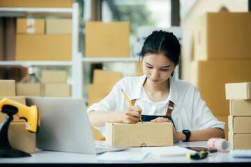 Online business owner writing customer address on a parcel box before shipping