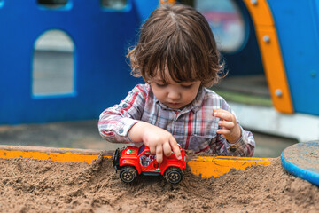 little boy playing in the sandbox with a car