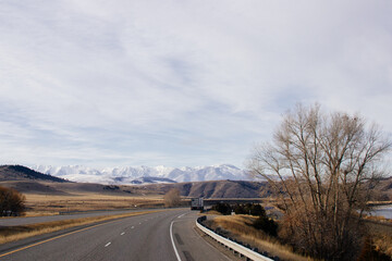 Beautiful landscape with a road among yellow dry grass and snow-covered mountains on the horizon.