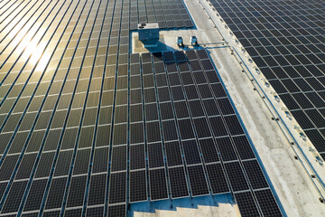 Aerial view of blue photovoltaic solar panels mounted on industrial building roof for producing...