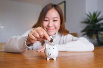 Portrait image of a young woman holding and putting coins into piggy bank for saving money concept