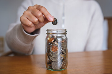 Fototapeta na wymiar Closeup image of a woman collecting and putting coins in a glass jar for saving money concept