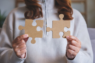 Closeup image of a woman holding and putting a piece of wooden jigsaw puzzle together