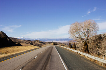 Fototapeta premium Beautiful landscape with a road among yellow dry grass and snow-covered mountains on the horizon.