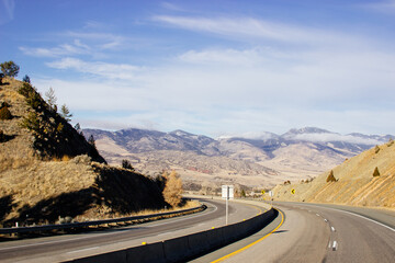 Steep highway in the mountains among huge rocks and high mountains on the horizon on a sunny day. Beautiful blue sky with clouds over mountains and asphalt road. USA highways