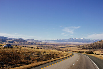 Fototapeta na wymiar Steep highway in the mountains among huge rocks and high mountains on the horizon on a sunny day. Beautiful blue sky with clouds over mountains and asphalt road. USA highways