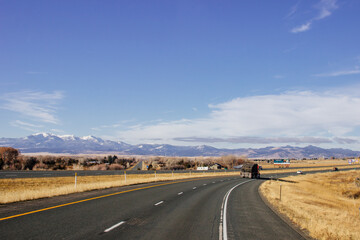 Steep highway in the mountains among huge rocks and high mountains on the horizon on a sunny day. Beautiful blue sky with clouds over mountains and asphalt road. USA highways