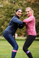 Two smiling mature women with resistance bands in park.