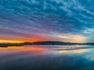 Fototapeta na wymiar Heavy cloud covered sunrise over the bay with colour and reflections