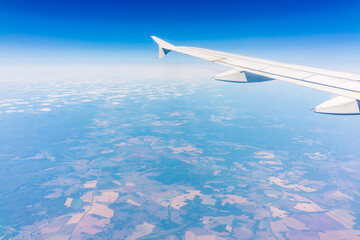Obraz premium Aerial view from airplane window above green ground. View from the airplane window with beautiful clouds at sunrise
