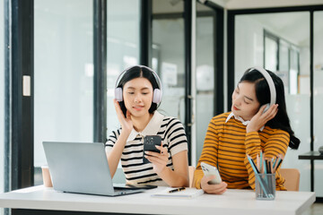 Two Attractive young Asian female college students working on the school project using laptop computer and tablet together, enjoy talking 