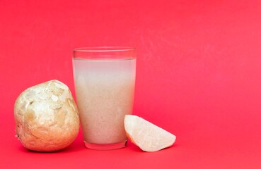 Closeup of Jicama or Mexican Turnip Juice in a Glass with Fruit Isolated on Red Background with Copy Space, Also Known as Yam Bean or Shank Aloo in Horizontal Orientation