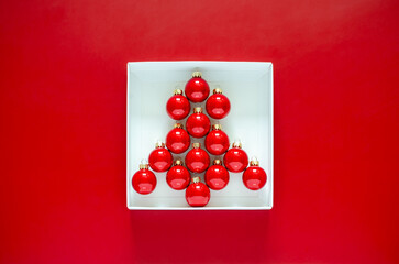 Red baubles set as Christmas tree shape put in white box on red background. Minimal Christmas holiday concept.