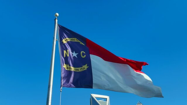 North Carolina flag waving against bright blue sky. Static aerial shot in downtown city in NC.