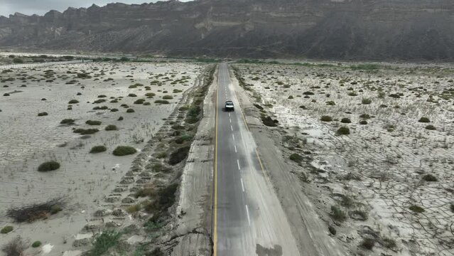 Tracking drone footage of Jeep car from the front on straight road in between valley and mountain Hingol Baluchistan