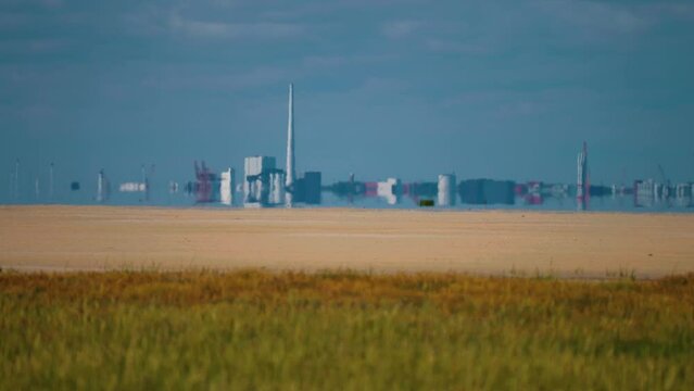 The contrast between nature and industry - a yellow wheat field and an industrial plant in the background on the Danish coast.