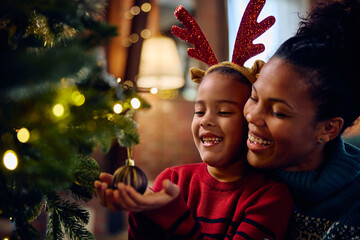 Happy black mother and daughter decorating Christmas tree.