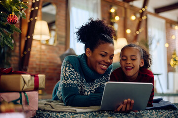 Happy black mother and daughter using digital tablet at Christmas at home.