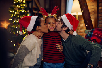 Happy black girl embracing her parents while they are kissing her at Christmas at home.
