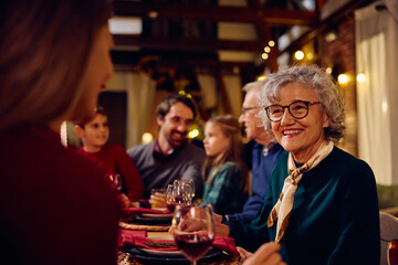 Happy senior woman enjoys in conversation while celebrating Christmas with her family at dining table.