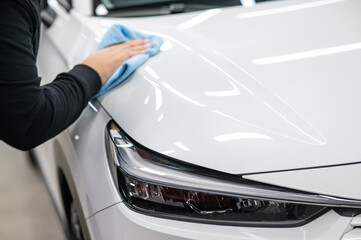 A mechanic wipes the body of a white car with a microfiber cloth. 