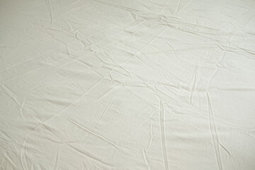 Crumpled bed sheet background texture. Light yellow fabric top view, light fabric