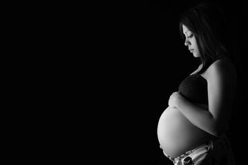 Young pregnant woman in profile holding her belly. Black and white, copy space. motherhood concept. Future mom.