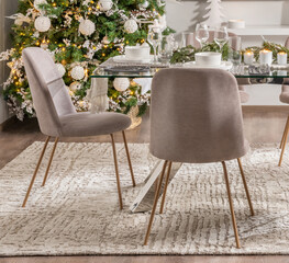 Modern Christmas Dinner Setting, Elegant Fabric Chairs and Festive Table with White Porcelain, Crystal Glassware, and Pine Garland, Illuminated by a Decorated Tree and Soft Candlelight, Holiday Table.