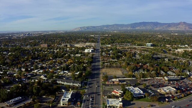 Dolly in tilt up aerial drone extreme wide landscape shot of the Salt Lake county valley covered in buildings, busy roads, and colorful autumn trees on a warm sunny fall evening in Utah