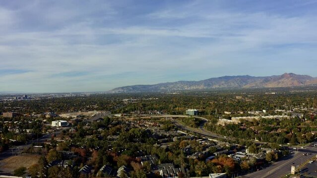 Right trucking rising aerial drone extreme wide landscape shot of the Salt Lake county valley covered in buildings, busy roads, and colorful autumn trees on a warm sunny fall evening in Utah