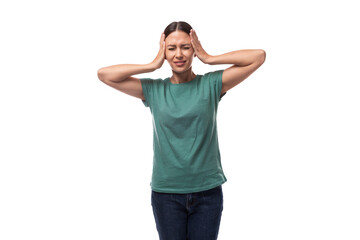 young beautiful brunette lady with a ponytail hairstyle is dressed in a green t-shirt and jeans feels a headache