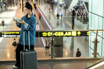 Young woman holding passport and ticket at airport terminal, looking for her gate or waiting for...
