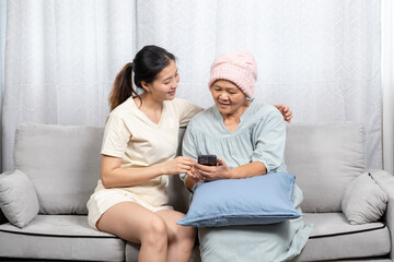 Happy Asian mother and daughter taking a selfie in the living room at home on the sofa on vacation with a bright smile. Happy Asian mother and daughter using smartphone at home.