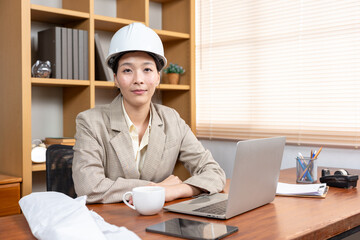 Portrait of a beautiful happy young engineer wearing a white hard hat. Using laptop computer in office in factory office, industrial professional working on vehicle design in modern factory.