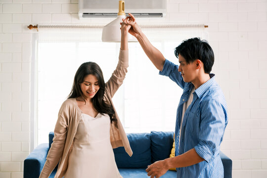 Attractive young Asian couples enjoy having a lovely romantic dance in the living room of the apartment. A family spends quality time together after moving into a new home. Image with copy space.