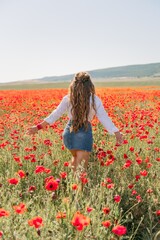 Woman poppies field. Back view of a happy woman with long hair in a poppy field and enjoying the beauty of nature in a warm summer day.