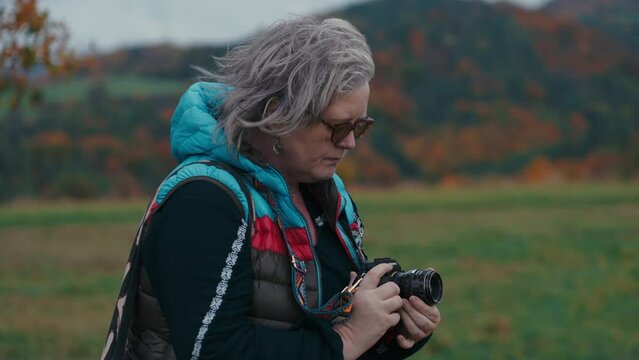 Close up shot of Female Photographer changing aperture in her camera, pressing a shutter and taking a picture of a beautiful windy autumn nature with orange leaves in the background. Sony FX3 in 4K