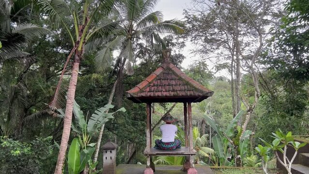 Tranquil Balinese Serenity: Young Male Tourist in Anjali Mudra Pose at Goa Gajah Temple Gazebo, Bali Rainforest View; Serene 4K Tripod Shot Ideal for Meditation Blogs and Spiritual Journeys