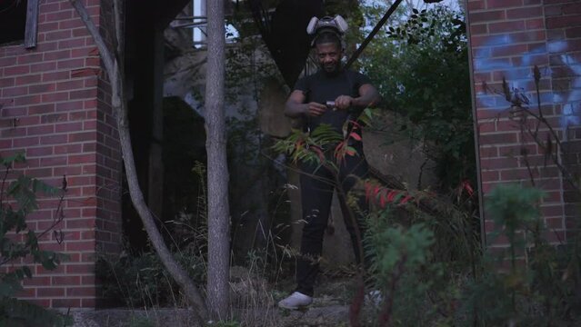 a black man with a gas mask on his head ignites a flare before placing the gas mask over his face in an abandoned  red brick building