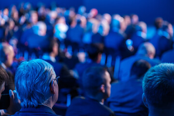 Businessmen listening to speaker giving presentation in illuminated auditorium at export forum 