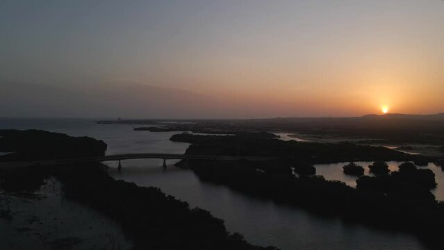 Drone moves to the right gaining altitude revealing a silhouetted bridges, mangrove forests, ocean on the horizon and mountains with the majestic sunset, Porlamar, Margarita Island, Venezuela