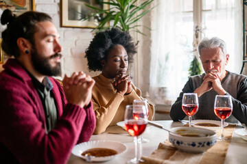 Happy multiethnic family praying before meal at home together. People religion concept