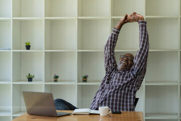 A senior African American man stretching arms raised relaxing at the office.