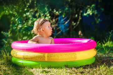 A cute little baby boy is playing with toys while bathing in a little colorful wading pool on meadow garden field outdoor. Summer time. Joy and happiness. Love and family © guruXOX